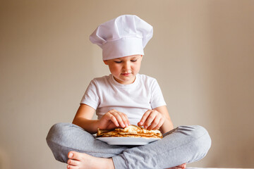 seven-year-old boy in a white T-shirt and white chef's cap plays with pancakes on a white background