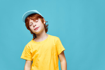 Red-haired boy eyes closed tilting his head to one side yellow t-shirt cap studio 