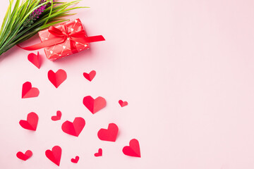 Valentines' day background. Red gift box with ribbon bow, wood red hearts shaped and flower composition greeting card for love isolated on pink background with copy space. Top View from above