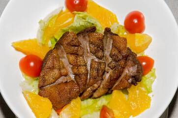 Roasted duck with fresh tomatoes, orange, herbs on a white plate. View from above