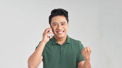 Portrait of an excited young man talking on mobile phone isolated over white background