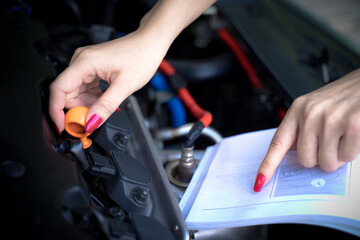 A woman fixes her car and opens a car manual to fix her car on a non-start day
