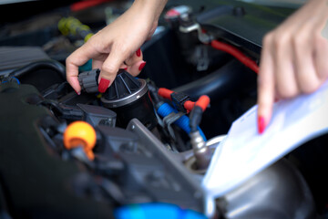 A woman fixes her car and opens a car manual to fix her car on a non-start day