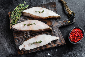 Raw fresh halibut fish steak on a wooden cutiing board. Black background. Top view