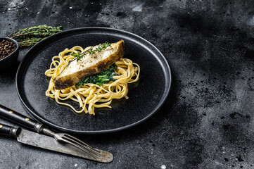Spaghetti pasta with Halibut fish steak and spinach. Black background. Top view. Copy space