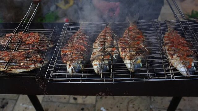 Dorado fish grilled over charcoal. Close-up shot cooking seafish with aromatic spices on barbecue grill plate. Baking roasting marinated delicious seafood. BBQ in summer garden outdoors in Cyprus