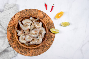 Raw shrimps or prawns in wooden plate with lime and red hot pepper ready for cooking. A bowl of fresh raw pacific white shrimp, ingredients for cooking, seafood. Top view, space for text.