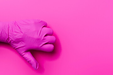 A hand of a paramedic in a pink glove shows a dislike on a pink background with side space. Thumb down.
