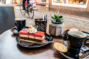 Coffee and dessert on a cafe street terrace. Cup of coffee, cookie and cake with whipped cream on the table close-up.