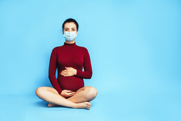 Pregnant girl in front of a blue background. Sports activities for pregnant women. Caring for the health of pregnant women. Medical mask on woman's face