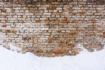 Grunge red dirty brick wall. Urban underground texture. Antique house exterior wall. Vintage rustic building architecture. Winter brick wall. Snow on the ground.