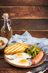 Breakfast with eggs, grilled sausage, green beans and toast on wooden background