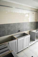 Lower custom kitchen cabinets installation with a furniture facades mdf. Gray modular kitchen from chipboard material on a various stages of installation. A frame furniture fronts mdf profile.