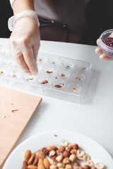Making homemade chocolate. Women's gloved hands sprinkle chocolate with rice balls. Plastic confectionery forms for sweets.