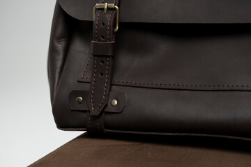 Details of brown men's shoulder leather bag for a documents and laptop on a brown chair with a white background. Mens leather brief case, messenger bags, leather satchel, handmade briefcase.