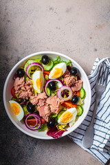 Tuna salad with egg, olives and vegetables in white bowl, dark background. Diet food concept.