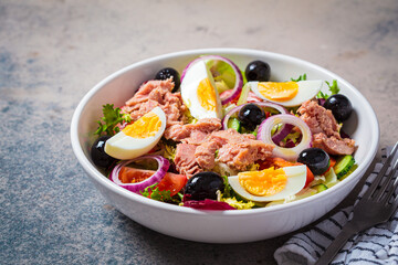 Tuna salad with egg, olives and vegetables in white bowl, dark background. Diet food concept.