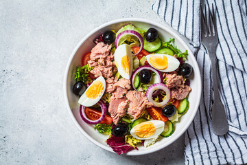 Tuna salad with egg, olives and vegetables in white bowl, white background. Diet food concept.