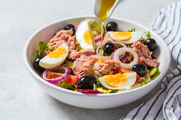 Tuna salad with egg, olives and vegetables in white bowl, white background. Diet food concept.