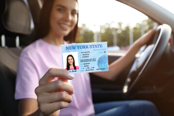 Happy young woman holding license while sitting in car, focus on hand. Driving school