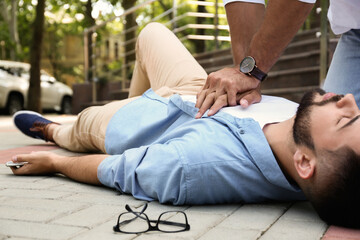 Passerby performing CPR on unconscious young man outdoors. First aid - Powered by Adobe