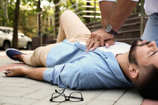 Passerby performing CPR on unconscious young man outdoors. First aid