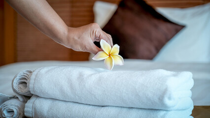Hands of hotel maid putting plumeria flower and towels on the bed in the luxury hotel room ready for tourist travel