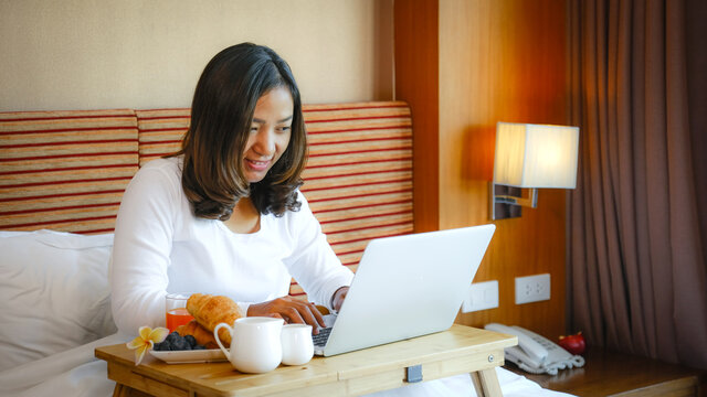 Picture of tourists used laptop and eating breakfast on the bed in the luxury hotel room, healthy food concept