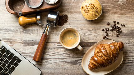 Coffee preparation on the wooden table. Espresso cup with portafilter filled with ground coffee.Muffin and croissant