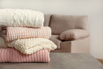 Stack of clean freshly laundered, neatly folded women's clothes on wooden table. Pile of shirts and sweaters on the table, white wall background. Copy space, close up, top view.