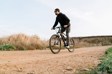 Naklejka premium Handsome unshaven guy in sunglasses riding his bicycle outdoors