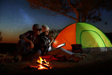 Couple with flashlight reading book near bonfire at night. Camping season