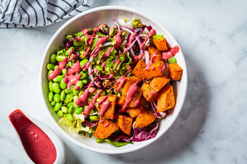Vegan salad bowl with baked sweet potato, edamame beans, nuts and pink beetroot dressing. Vegan...