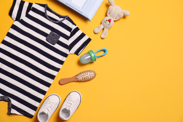 Flat lay composition with baby clothes and accessories on yellow background. Space for text