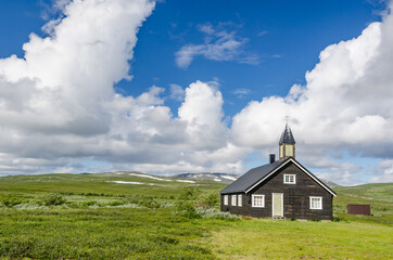 Fototapeta na wymiar Small black wooden church on green hills Norway tundra