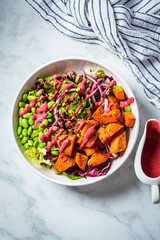 Vegan salad bowl with baked sweet potato, edamame beans, nuts and pink beetroot dressing. Vegan food concept.