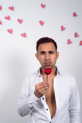 Young man holding a red rose with many paper hearts flying behind him, white background. Concept of love, Valentine