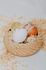 Three easter eggs in the basket on white background with sawdust around. Happy Easter card. Easter eggs decoration with lace border and rope. Golden easter egg.
