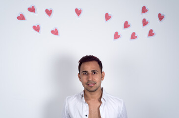 Young man looking happy with many paper hearts flying behind him, white background. Concept of love, Valentine