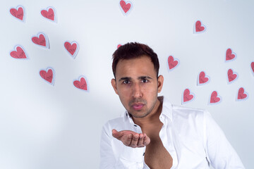 Young man blowing on his hand with many paper hearts flying behind him, white background. Concept of spreading love, Valentine 