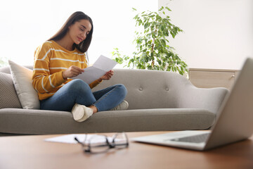Woman reading letter on sofa at home