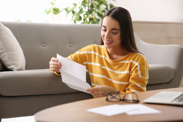 Young woman reading paper letter at home