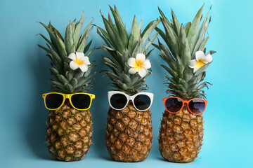 Funny pineapples with sunglasses and plumeria flowers on light blue background. Creative concept