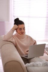 Beautiful young woman with laptop relaxing at home. Cozy atmosphere