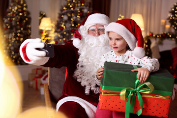Fototapeta na wymiar Santa Claus and little girl taking selfie in room decorated for Christmas