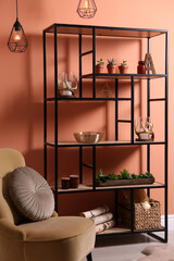 Armchair near shelving with different decor, houseplants and firewood in room. Interior design