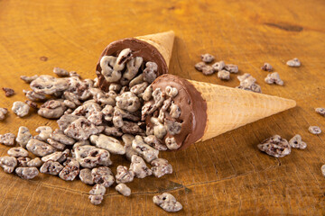 Sweet, ice cream cone filled with chocolate and cream with chocolate flakes, on rustic wood, selective focus.