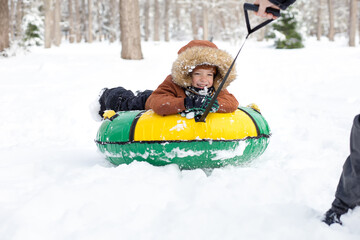 father rides son on snow tube in winter, baby close-up, happy face