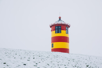Small lighthouse in red and yellow. Lighthouse on a dike on the North Sea. Light tower with snow in winter