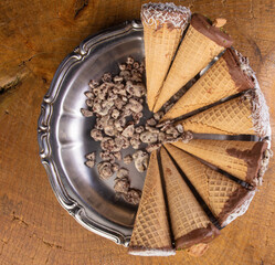 Sweet, ice cream cone filled with chocolate and cream with chocolate flakes, on a tray on rustic wood, top view.